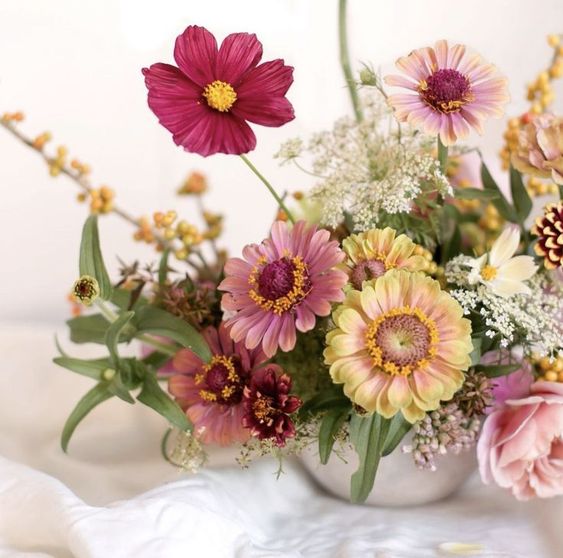 a bright wedding centerpiece of pink and burgundy cosmos, yellow and pink blooms, greenery and fillers is a cool idea for summer or fall