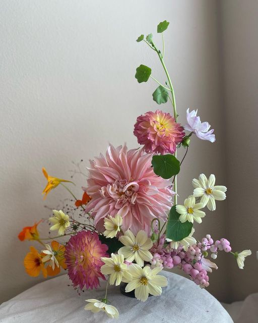 a bright wedding centerpiece of pink dahlias, orange blooms, yellow cosmos and greenery is a cool idea for the summer