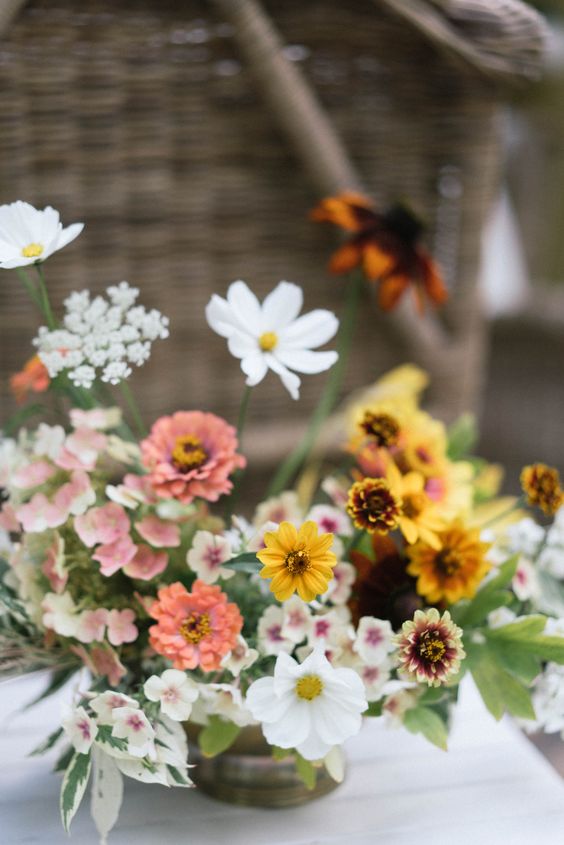 a bright wedding centerpiece of white cosmos, marigolds, pink and white fillers and blooms for summer weddings