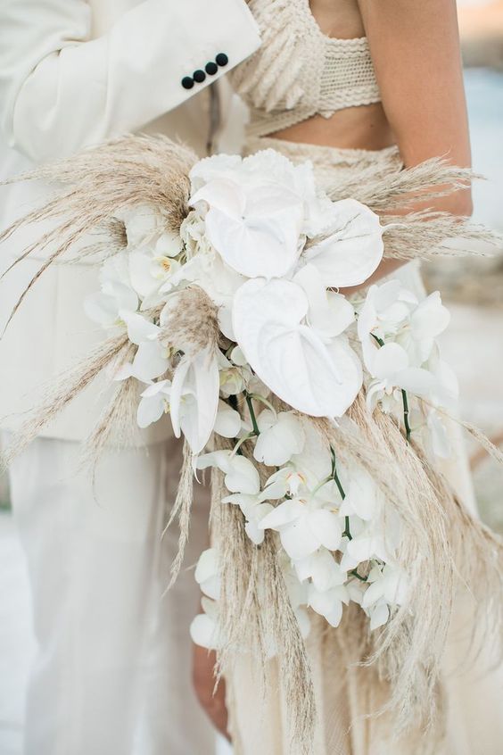 a cascading white wedding bouquet of anthuriums, orchids and pampas grass is a cool idea for a boho tropical wedding