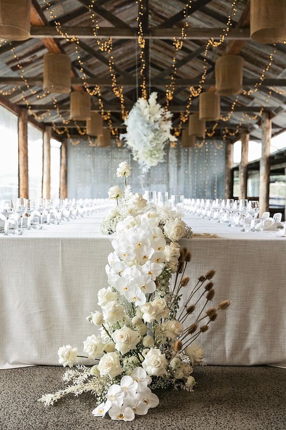 a cascading white wedding centerpiece of roses, orchids, white leaves and some dried touches is a cool and refined idea