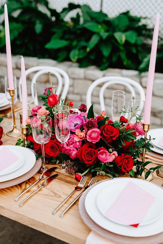 a chic and bold wedding centerpiece of red roses, pink and red ranunculus, anemones and lots of greenery for a bold fall or winter wedding