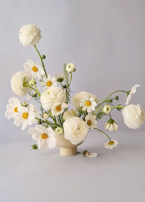 a chic modern white wedding centerpiece of ranunculus and cosmos is a cool and catchy idea for a wedding