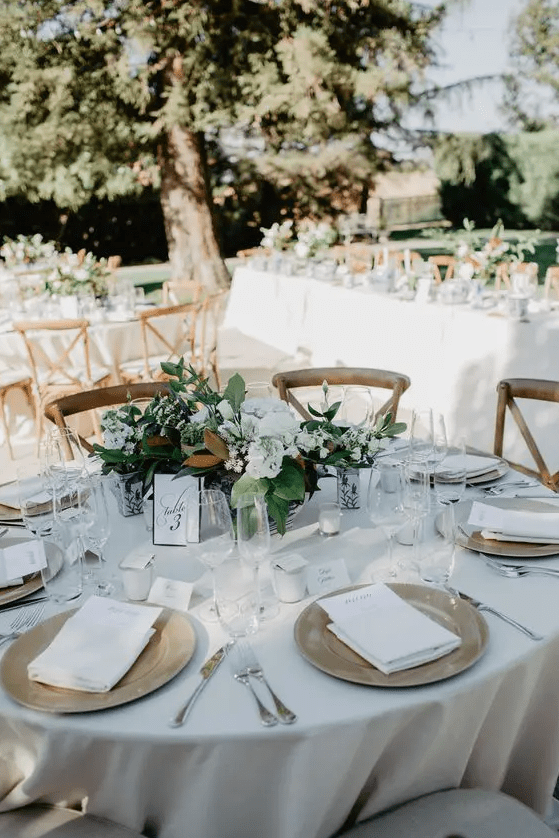 a chic neutral winter wedding tablescape with a white tablecloth and napkins, white blooms and greenery, candles and magnolia leaves