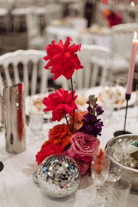 a colorful modern wedding centerpiece of red roses, purple and pink blooms and a disco ball for a modern celebration