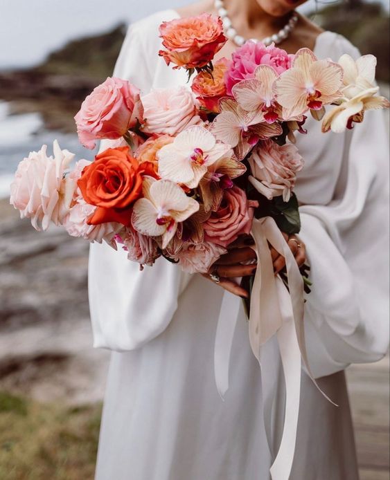 a colorful wedding bouquet of orange, pink and blush roses, blush orchids and some peonies is amazing for a modern bride