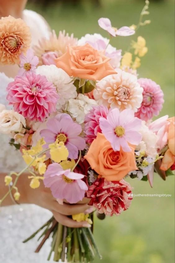 a colorful wedding bouquet of orange, white and pink dahlias, pink cosmos and some orange roses for a summer wedding