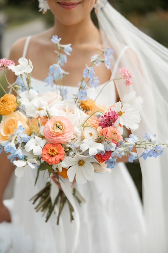 a colorful wedding bouquet of pink ranunculus, yellow roses, white cosmos and some blue fillers for summer
