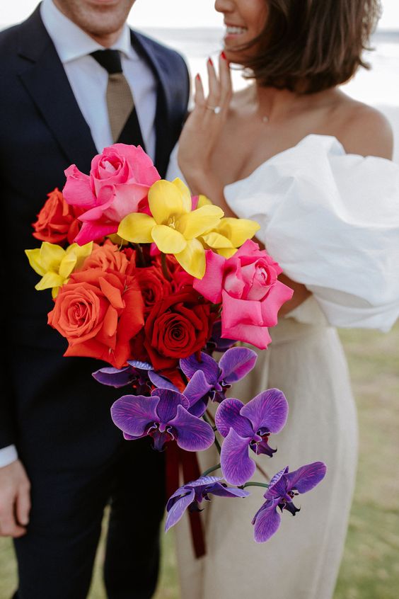 a colorful wedding bouquet of red, burgundy and hot pink roses, yellow blooms and cascading violet orchids is amazing