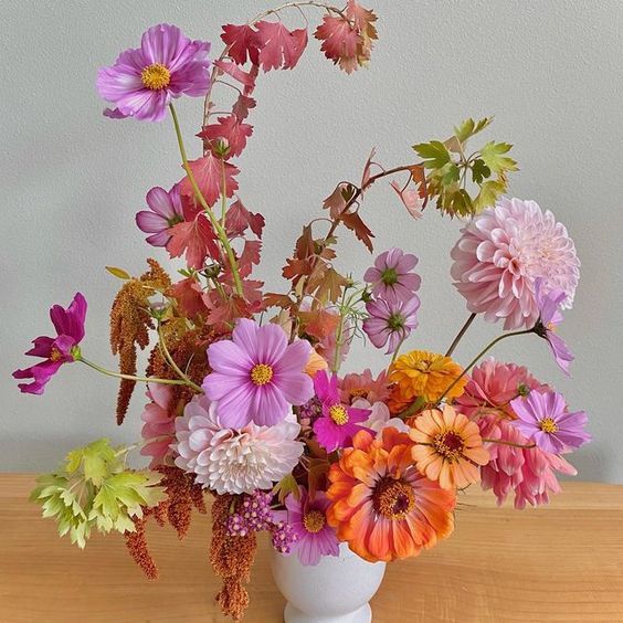 a colorful wedding centerpiece of hot pink cosmos, orange and rust mumes and some bright leaves for summer or fall
