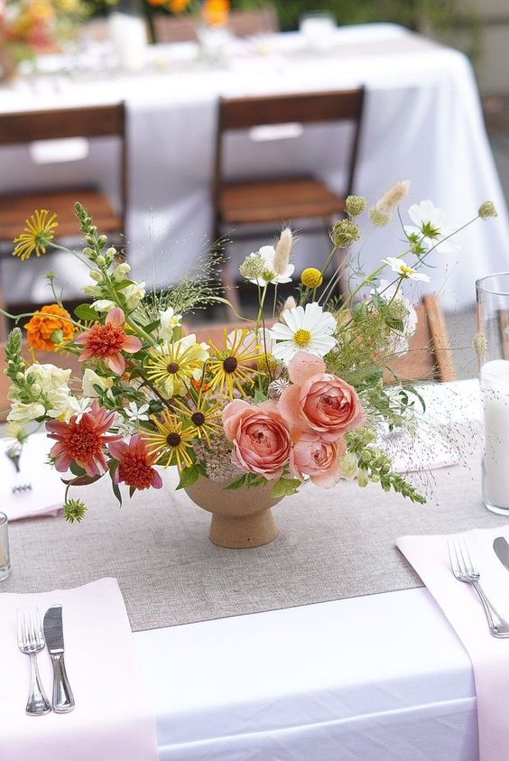 a colorful wedding centerpiece of pink roses, yellow and corla blooms, white cosmos and grasses plus greenery