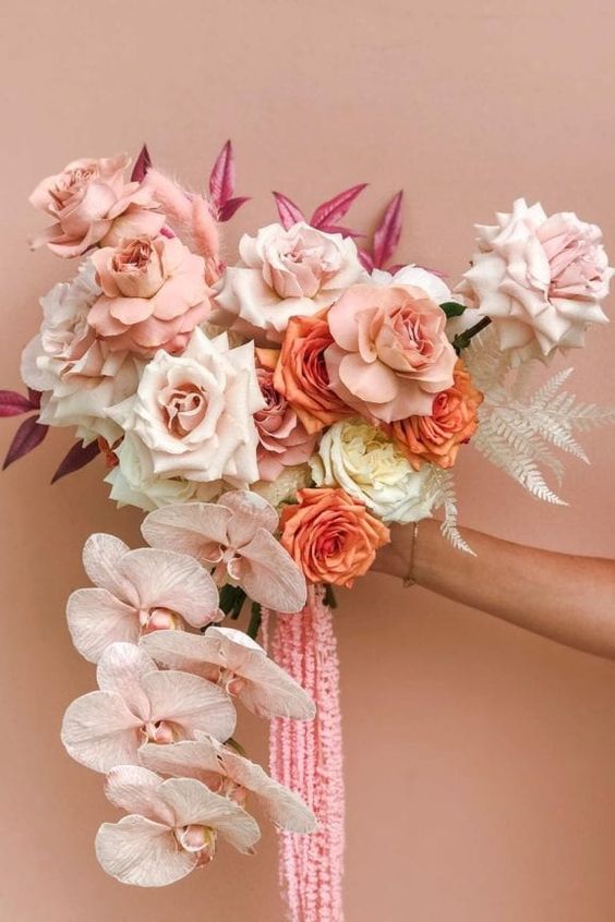 a delicate cascading wedding bouquet of blush and orange roses and blush orchids, pink amaranthus and pink leaves