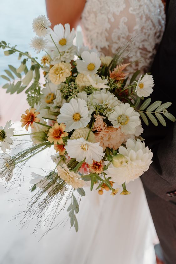 a dimensional wedding bouquet of white cosmos, dahlias, yellow and blush blooms and fillers and some greenery
