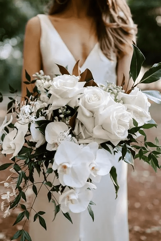 a dimensional white wedding bouquet with roses, orchids and other blooms plus greenery and magnolia leaves