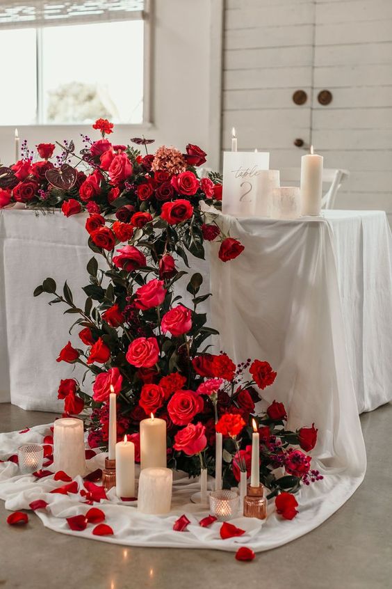 a fantastic red and burgundy rose cascading wedding centerpiece with some anthuriums, greenery and candles is adorable