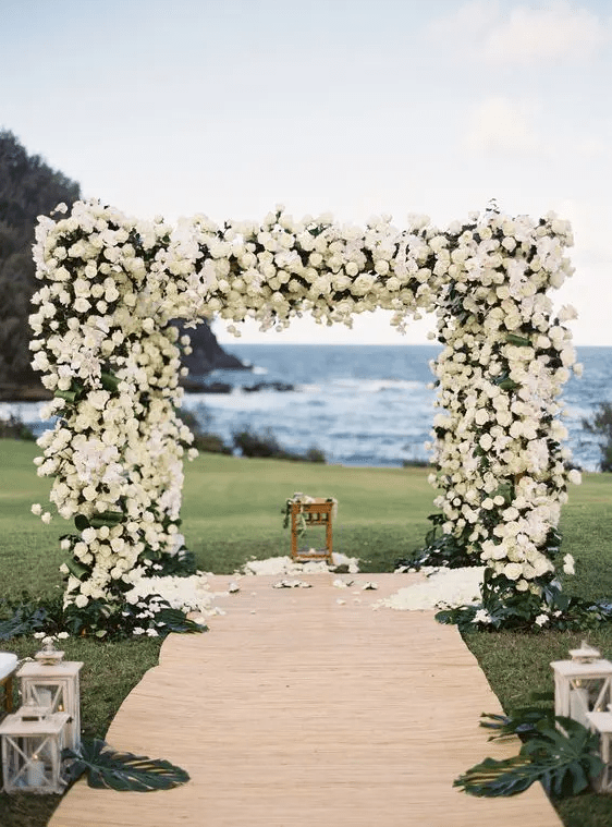 a floral arbor covered with white roses completely and a backdrop of the ocean look wow