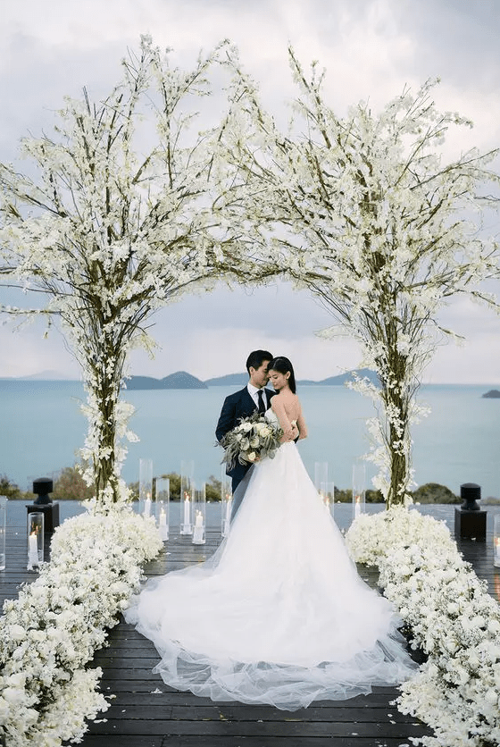 a floral arch composed of two trees and white blooms and white blooms to line up the aisle