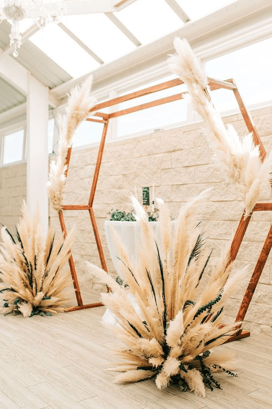a gorgeous boho hexagon wedding arch decorated with pampas grass and greenery is a lovely idea for a boho wedding