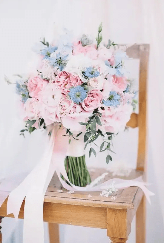 a gorgeous wedding bouquet of pink roses and peonies and some blue blooms and long blush ribbons is amazing