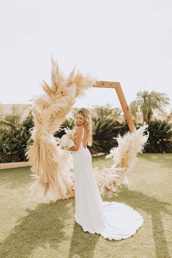 a hexagon wedding arch with pampas grass and fronds is a cool idea for a boho wedding in any season