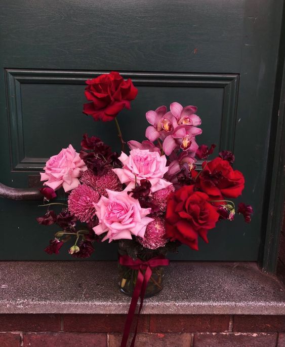 a jewel-tone wedding bouquet of pink and red roses, pink orchids, burgundy sweet peas and some pink fillers for a fall wedding