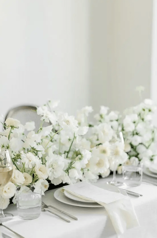 a large and lush white wedding centerpiece of ranunculus and cosmos is adorable for a spring or summer wedding