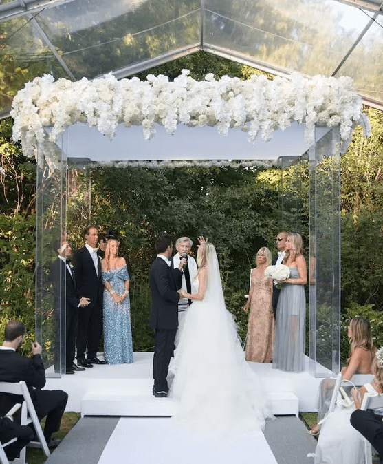 a large lucite wedding arbor topped with very lush white blooms is a beautiful idea for a modern edgy wedding with a lux feel