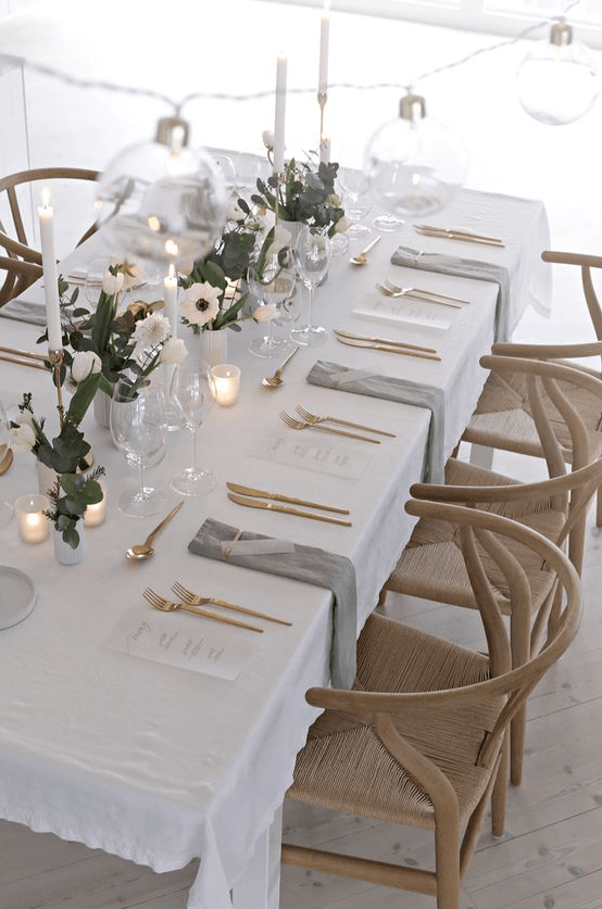 a lovely Scandinavian minimalist tablescape with greenery and white blooms, candles, gold cutlery and grey napkins