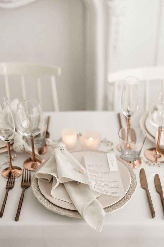 a lovely and airy Scandinavian wedding tablescape with copper cutlery and glasses, candles, neutral linens and plates