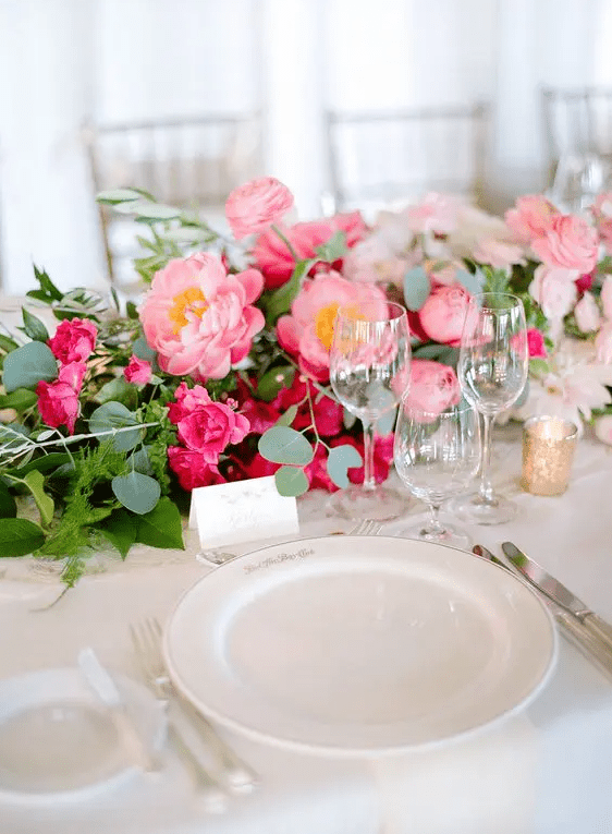 a lovely ombre pink wedding centerpiece with ranunculus, peonies and roses plus greenery and candles is amazing