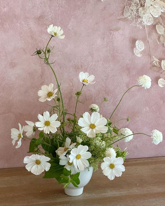 a lovely white wedding centerpiece of cosmos and some fillers plus greenery is cool for spring and summer
