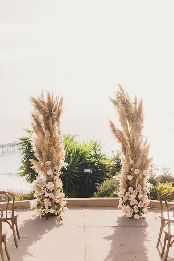 a lush boho wedding altar of pampas grass, blush and white roses and a cool tropical view is wow