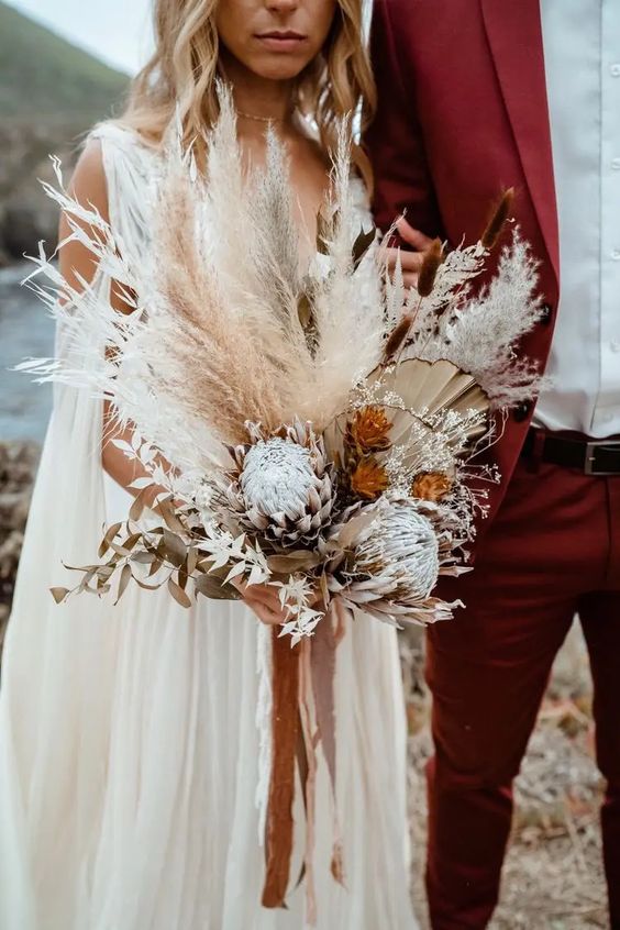 a lush boho wedding bouquet of king proteas, fronds, dried leaves and pampas grass is amazing