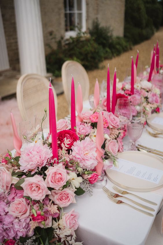 a lush cascading wedding centerpiece of pink and red peonies, pink roses and hydrangeas plus hot and light pink candles