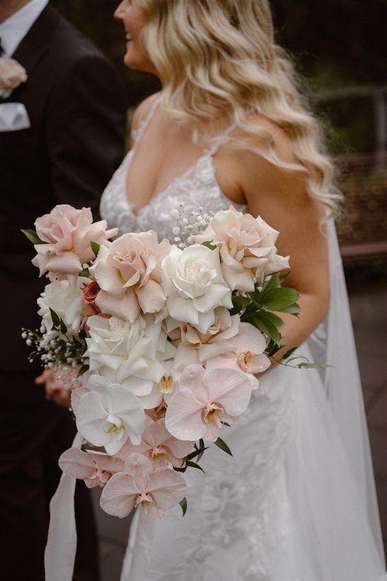 a lush modern wedding bouquet of white and blush roses, blush orchids and baby's breath plus some greenery is wow
