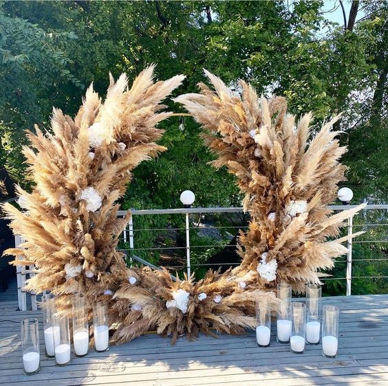 a lush pampas grass altar with some white blooms and candles in glasses is a cool wedding decor idea