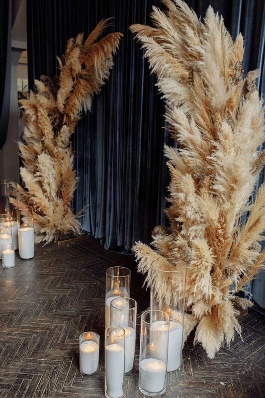 a lush pampas grass wedding altar with some candles brings an outdoor feel inside and it looks absolutely amazing