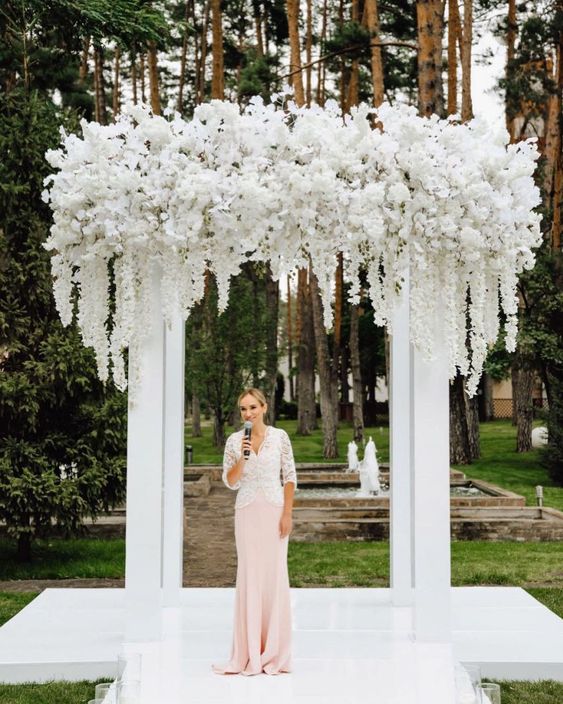a lush wedding chuppah with lots of white blooms of all kinds on top and some hanging white flowers is a chic idea for a wedding