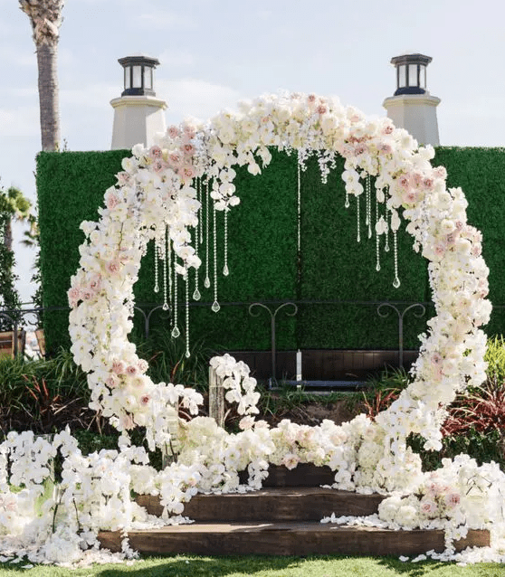 a luxurious circle floral arch with white and pink blooms and hanging crystals plus petals all around