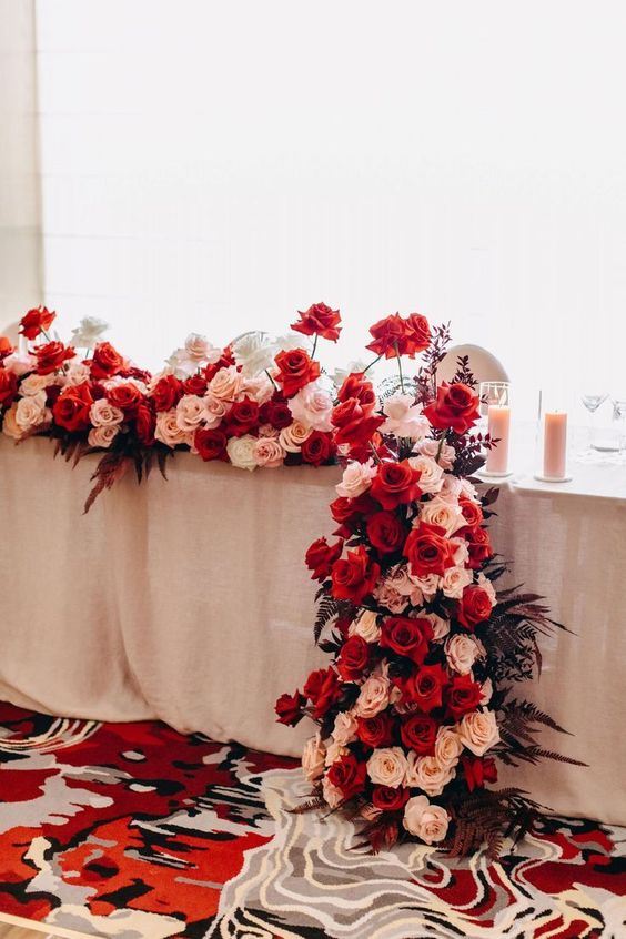 a luxurious rose wedding centerpiece of blush, red and white roses and dark leaves is a stylish and catchy decor idea