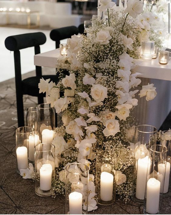 a luxurious white cascading wedding centerpiece of roses, orchids and baby's breath plus candles right on the wall