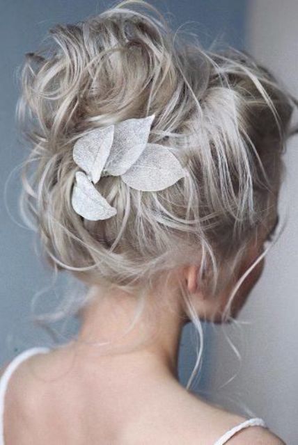 a messy wavy updo imitating a top knot, with a bump on top and fabric leaves that remind of lunaria pieces is amazing