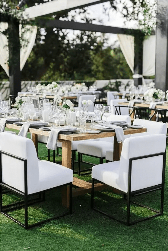 a modern lux wedding reception space with wooden tables, neutral linens, white blooms and candles plus chic upholstered chairs