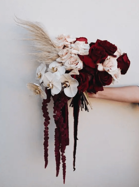 a moody wedding bouquet of burgundy and blush roses, white orchids, pampas grass, amaranthus is a chic and refined wedding idea