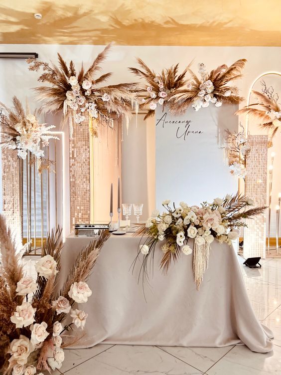 a neutral boho cascading wedding centerpiece of white and blush roses and fronds is a stunning idea, and matching arrangements echo with it