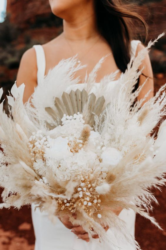 a neutral boho wedding bouquet of pampas grass, baby’s breath, fronds and white roses is a chic idea for a boho celebration