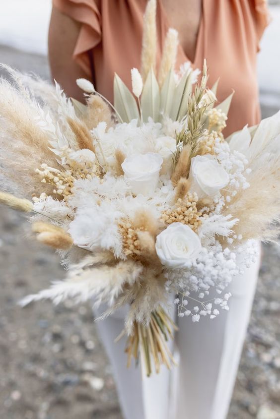 a neutral wedding bouquet of pampas grass, white roses, baby's breath and some fronds and grasses