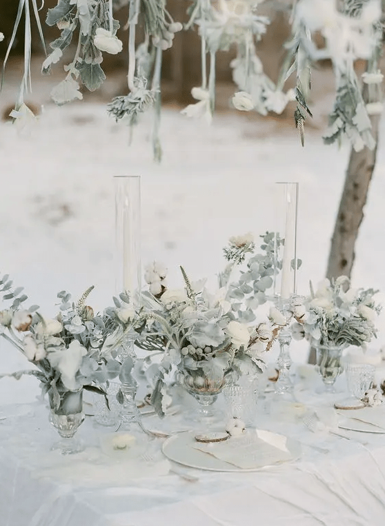 a neutral winter wedding tablescape styled with pale greenery and white blooms and the same over the table, neutral plates and menus