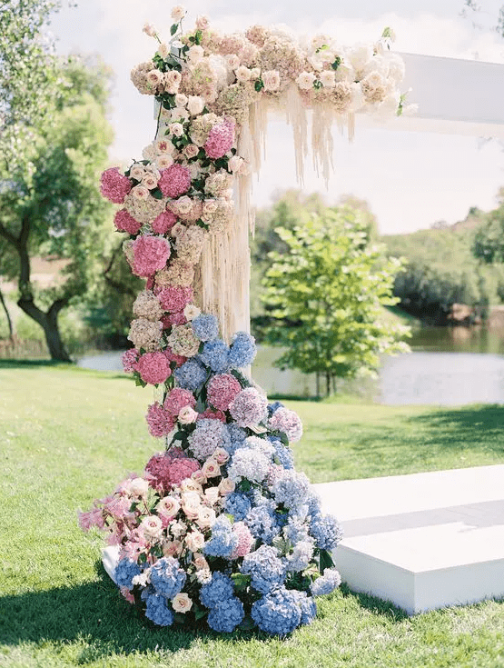 a pastel wedding arch done with white and blush roses and blue, pink and blush hydrangeas plus some cascading elements