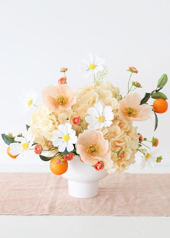 a pastel wedding centerpiece of peachy hydrangeas and poppies, white cosmos, some citrus is amazing for summer